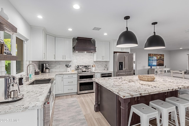 kitchen with a kitchen island, white cabinetry, sink, custom exhaust hood, and stainless steel appliances