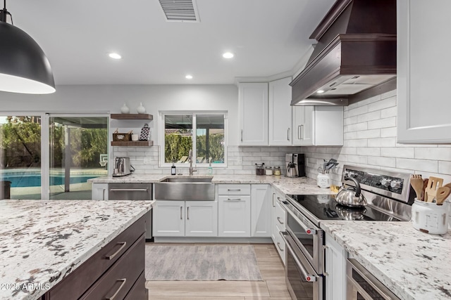 kitchen with premium range hood, white cabinetry, sink, hanging light fixtures, and double oven range