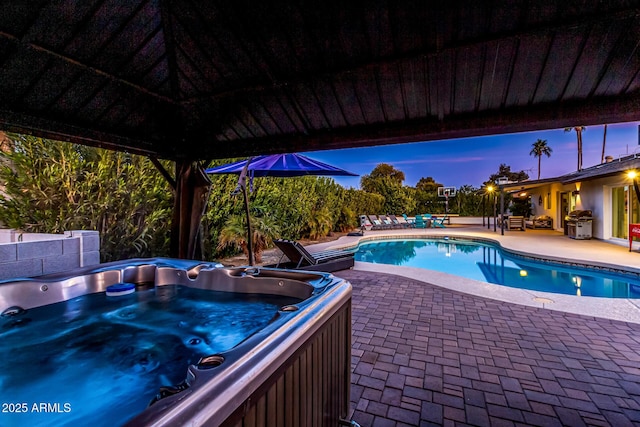 pool at dusk featuring area for grilling, a hot tub, and a patio