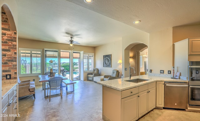 kitchen with light stone countertops, ceiling fan, stainless steel appliances, sink, and light tile floors