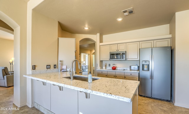 kitchen with light stone countertops, a kitchen bar, stainless steel appliances, sink, and light tile floors