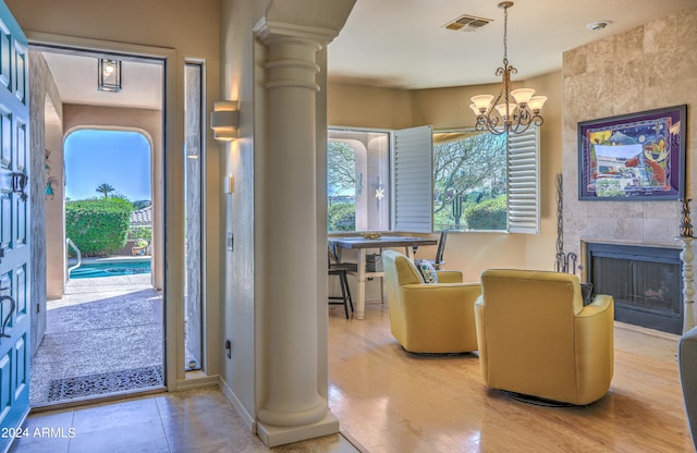 interior space with light wood-type flooring, a chandelier, ornate columns, and a fireplace