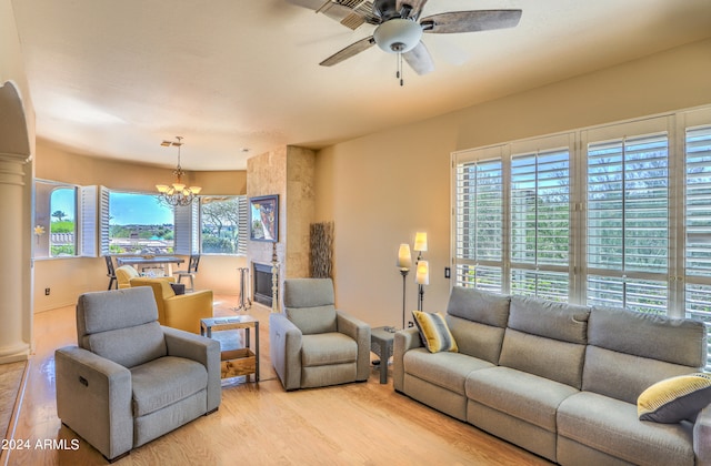 living room with light hardwood / wood-style floors, ceiling fan with notable chandelier, and a fireplace