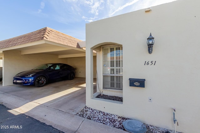 property entrance featuring an attached carport, mansard roof, a shingled roof, and stucco siding