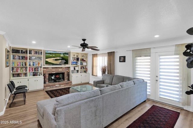 living room with ceiling fan, light hardwood / wood-style floors, a brick fireplace, a textured ceiling, and french doors