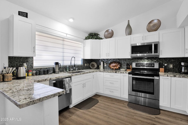 kitchen with sink, appliances with stainless steel finishes, white cabinets, vaulted ceiling, and kitchen peninsula