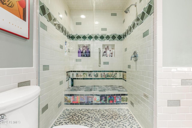 bathroom with tile walls, a wainscoted wall, a stall shower, and toilet