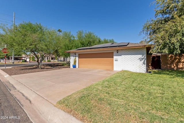 view of front of property featuring driveway, roof mounted solar panels, an attached garage, a front yard, and brick siding