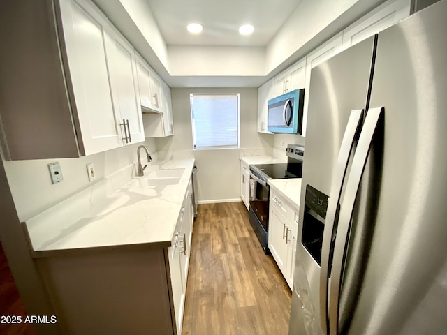 kitchen with white cabinets, light stone counters, wood finished floors, stainless steel appliances, and a sink