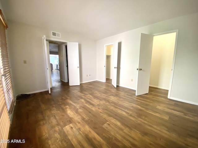 unfurnished bedroom featuring dark wood-style floors, baseboards, visible vents, and a walk in closet