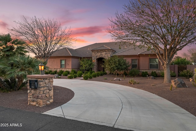 view of front of property featuring stone siding, fence, driveway, and stucco siding