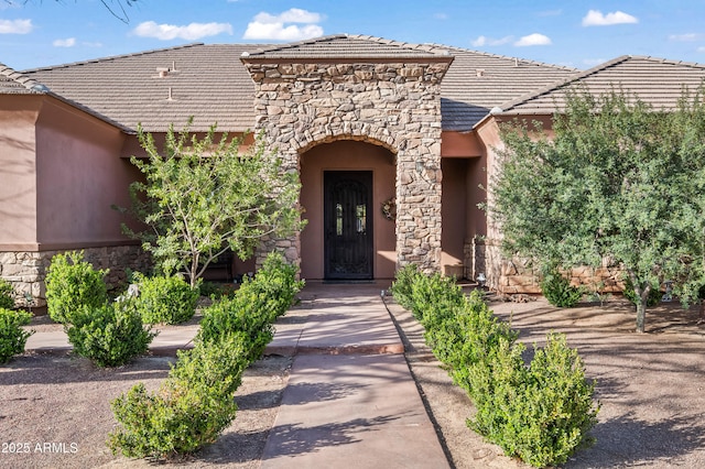 entrance to property featuring stone siding, stucco siding, and a tiled roof