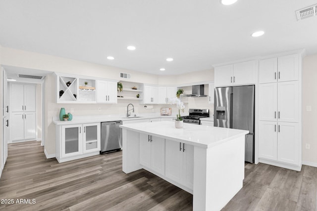kitchen with stainless steel appliances, wall chimney range hood, open shelves, a sink, and white cabinetry