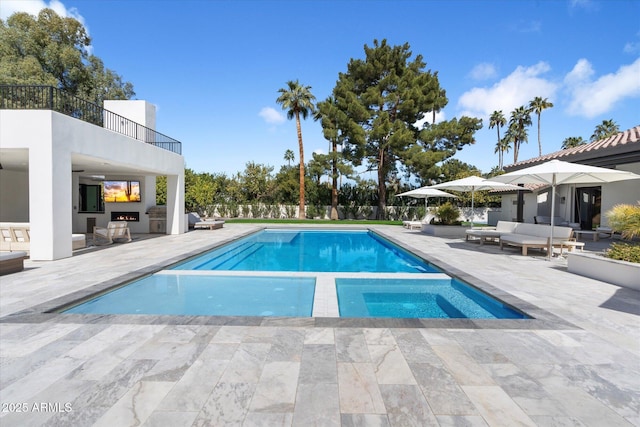 view of pool with an outdoor living space with a fireplace, a patio area, fence, and a pool with connected hot tub