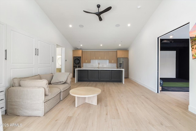 living area featuring baseboards, washer / clothes dryer, light wood-type flooring, high vaulted ceiling, and recessed lighting