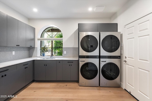 laundry room featuring stacked washer and dryer, light wood-style floors, cabinet space, and a sink