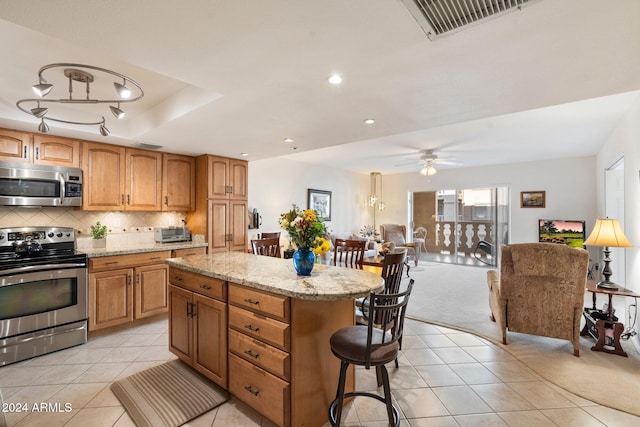 kitchen with ceiling fan, light tile patterned floors, a kitchen island, light stone counters, and stainless steel appliances