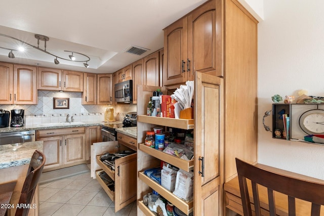 kitchen featuring backsplash, rail lighting, light tile patterned floors, appliances with stainless steel finishes, and light stone counters