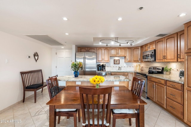 kitchen with light stone countertops, appliances with stainless steel finishes, tasteful backsplash, a kitchen island, and light tile patterned flooring