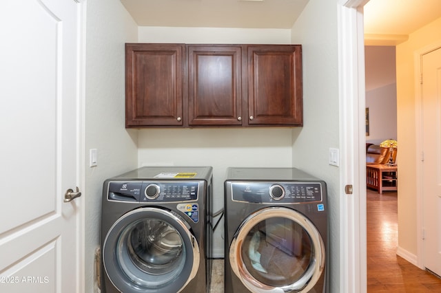 washroom with wood finished floors, washing machine and clothes dryer, and cabinet space