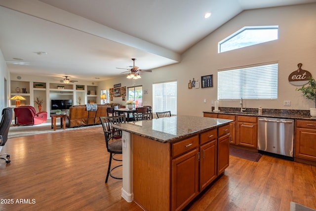 kitchen with wood finished floors, a sink, stainless steel dishwasher, brown cabinetry, and a kitchen bar