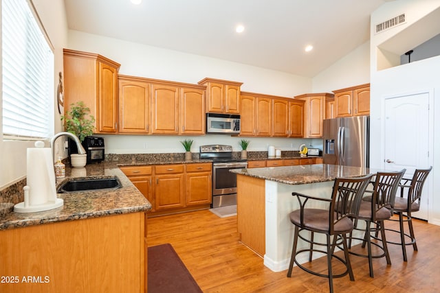 kitchen with appliances with stainless steel finishes, a kitchen breakfast bar, a center island, light wood-style floors, and a sink