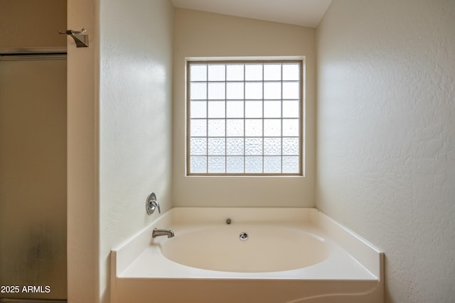 bathroom featuring vaulted ceiling, a textured wall, plenty of natural light, and a garden tub