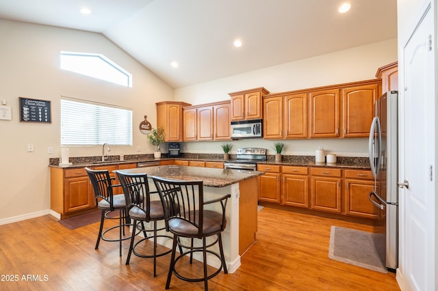 kitchen featuring stainless steel appliances, brown cabinetry, a kitchen island, light wood-type flooring, and a kitchen breakfast bar