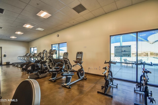 exercise room with a high ceiling, a drop ceiling, visible vents, and baseboards