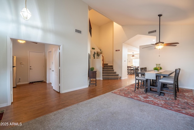 dining space with high vaulted ceiling, visible vents, stairway, and wood finished floors