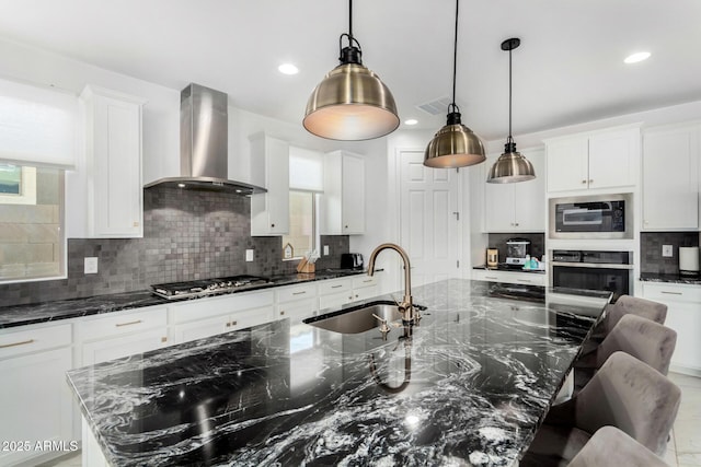 kitchen with wall chimney exhaust hood, sink, stainless steel gas cooktop, dark stone countertops, and a large island