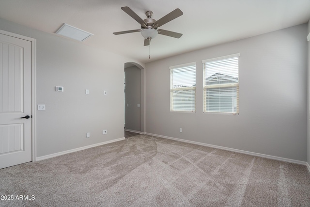 carpeted spare room with ceiling fan, arched walkways, and baseboards