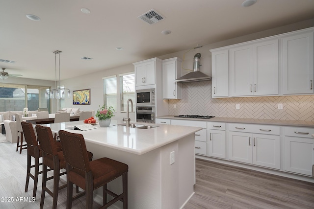 kitchen featuring wall chimney exhaust hood, visible vents, appliances with stainless steel finishes, a sink, and a kitchen breakfast bar