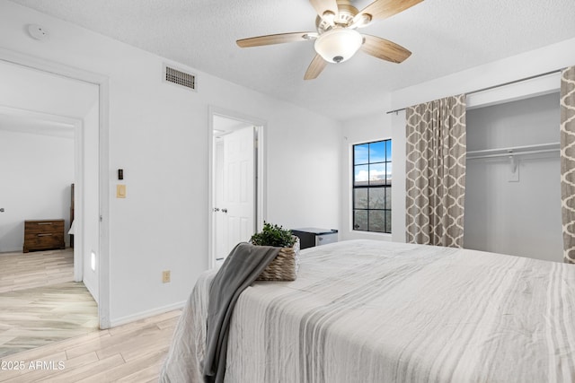 bedroom with ceiling fan, light hardwood / wood-style flooring, a closet, and a textured ceiling