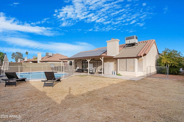 rear view of house featuring a fenced in pool, a lawn, solar panels, and central air condition unit