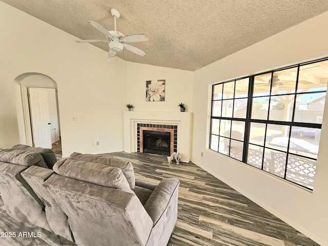 living room with wood-type flooring, vaulted ceiling, a textured ceiling, ceiling fan, and a tiled fireplace