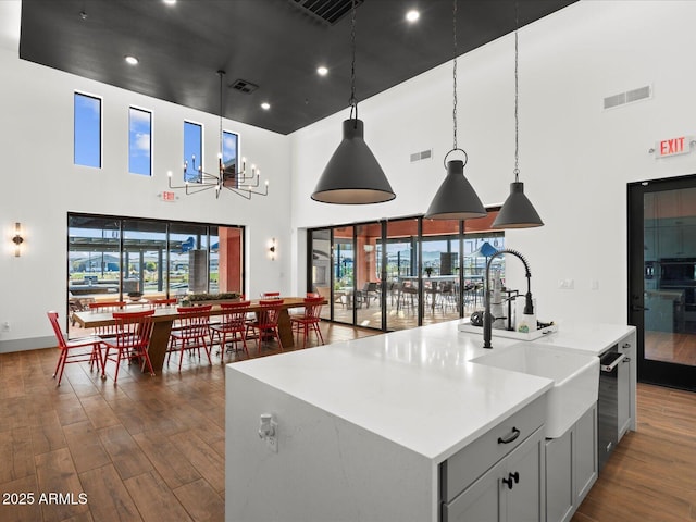 kitchen featuring a sink, a towering ceiling, dark wood finished floors, light countertops, and pendant lighting