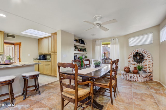 dining room featuring a skylight, ceiling fan, a fireplace, and light tile patterned floors