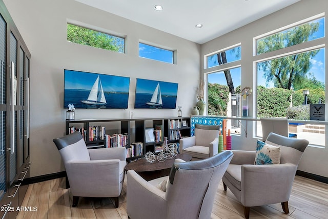 living area with recessed lighting, wood finished floors, a towering ceiling, and baseboards