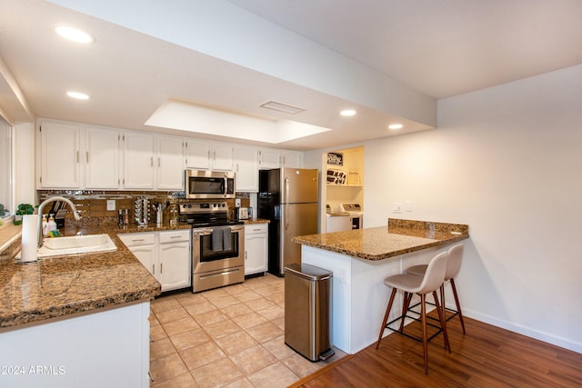 kitchen with visible vents, a peninsula, stainless steel appliances, white cabinetry, and a sink