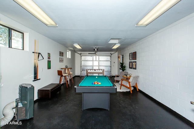 rec room with a garage, concrete block wall, pool table, and a dark floor