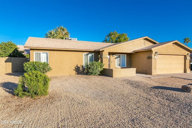 ranch-style home featuring an attached garage, roof with shingles, fence, and stucco siding