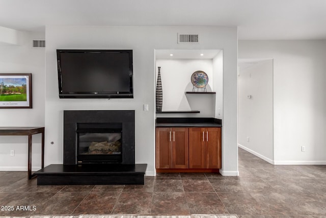 unfurnished living room with baseboards, visible vents, and a glass covered fireplace