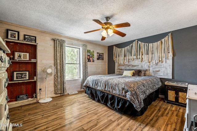 541 W Deuce Of Clubs, Show Low, AZ 85901 - bedroom featuring wood finished floors, a textured ceiling, visible vents, a ceiling fan, and wooden walls