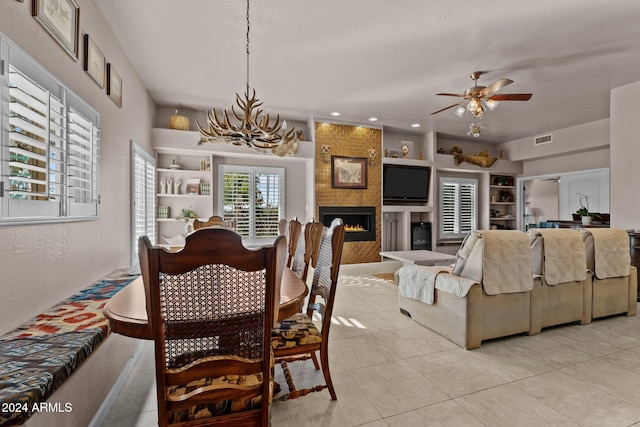 tiled dining space with built in features, ceiling fan with notable chandelier, and a fireplace