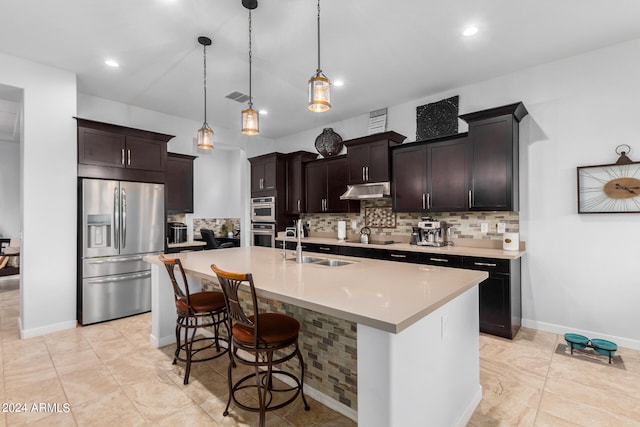 kitchen with an island with sink, tasteful backsplash, stainless steel appliances, decorative light fixtures, and sink