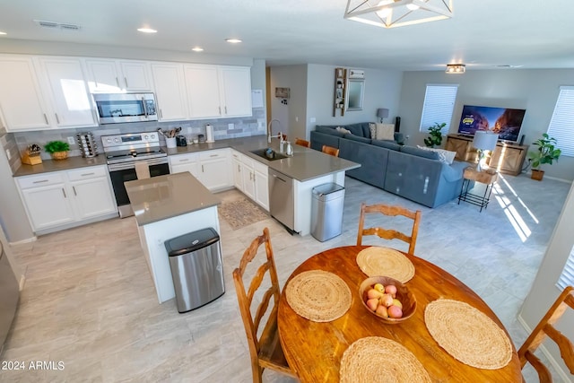 kitchen with stainless steel appliances, white cabinets, a center island, kitchen peninsula, and decorative backsplash