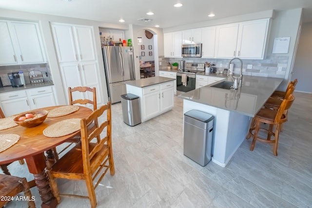 kitchen with sink, white cabinets, kitchen peninsula, decorative backsplash, and appliances with stainless steel finishes