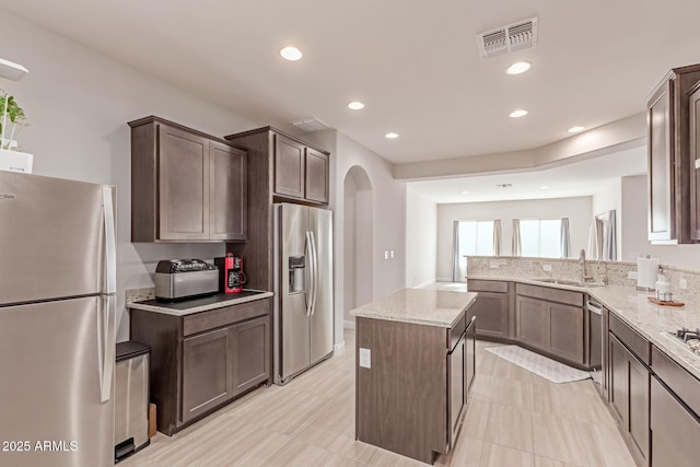 2881 N Riverside Dr, Florence, AZ 85132 - kitchen featuring appliances with stainless steel finishes, a sink, light stone counters, dark brown cabinetry, and arched walkways