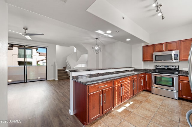 kitchen featuring ceiling fan, dark stone countertops, appliances with stainless steel finishes, decorative light fixtures, and kitchen peninsula